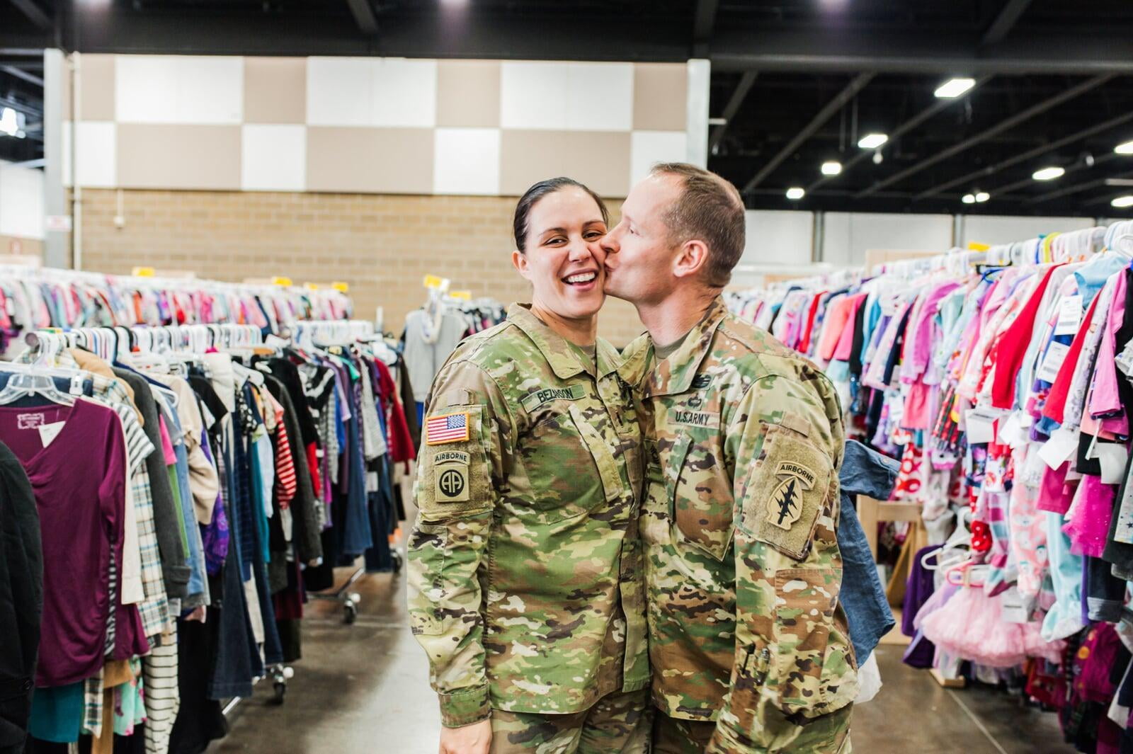 A military husband in camo kisses his military wife, also in camo, at the JBF sale in Tacoma Washington.